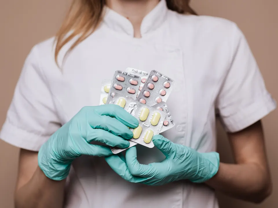 Medewerker in wit uniform met groene handschoenen houdt strips tabletten vast