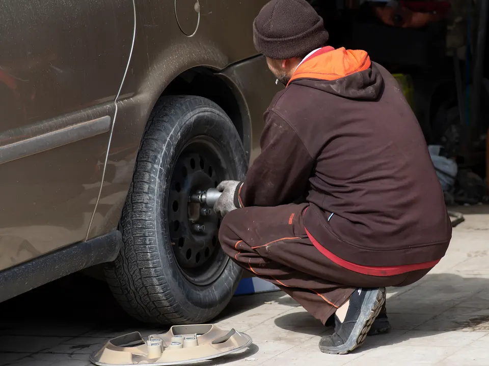 Monteur hurkt bij een auto en draait met een slagmoersleutel een wiel los