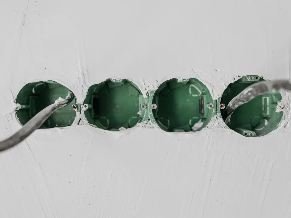 Vier groene inbouwdozen in een witte muur met aangesloten leidingen, klaar voor stopcontacten