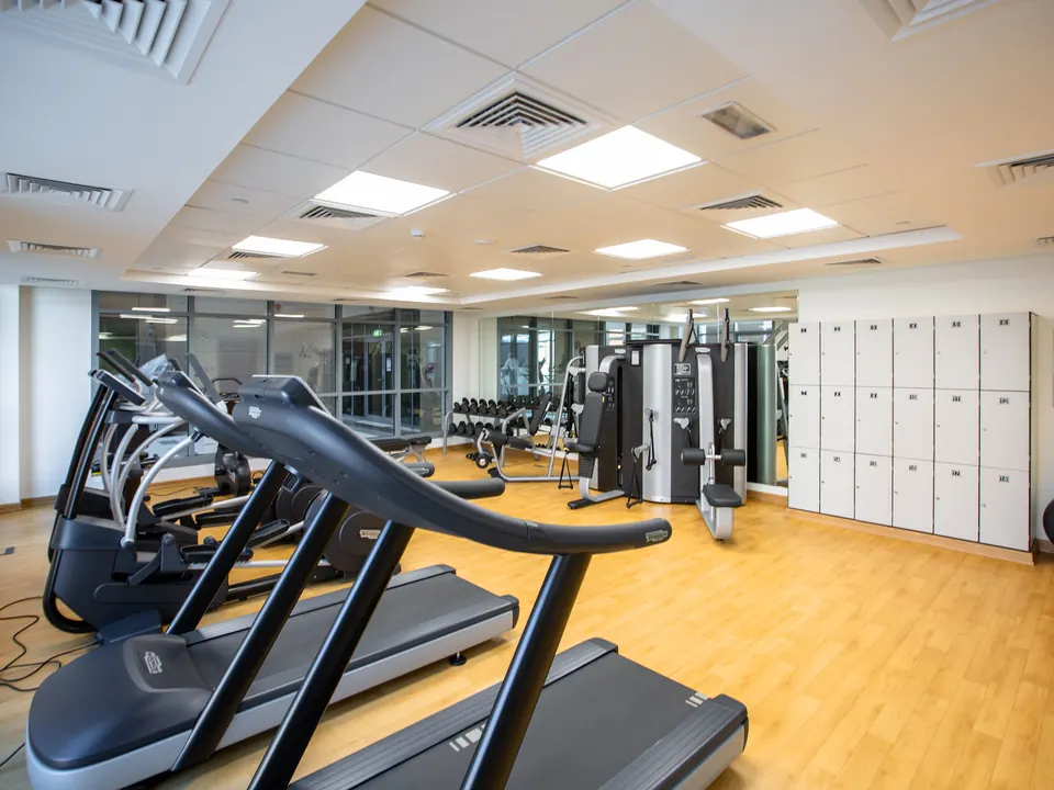 Lichte sportschool met rij loopbanden, krachtapparaten, halters en lockers