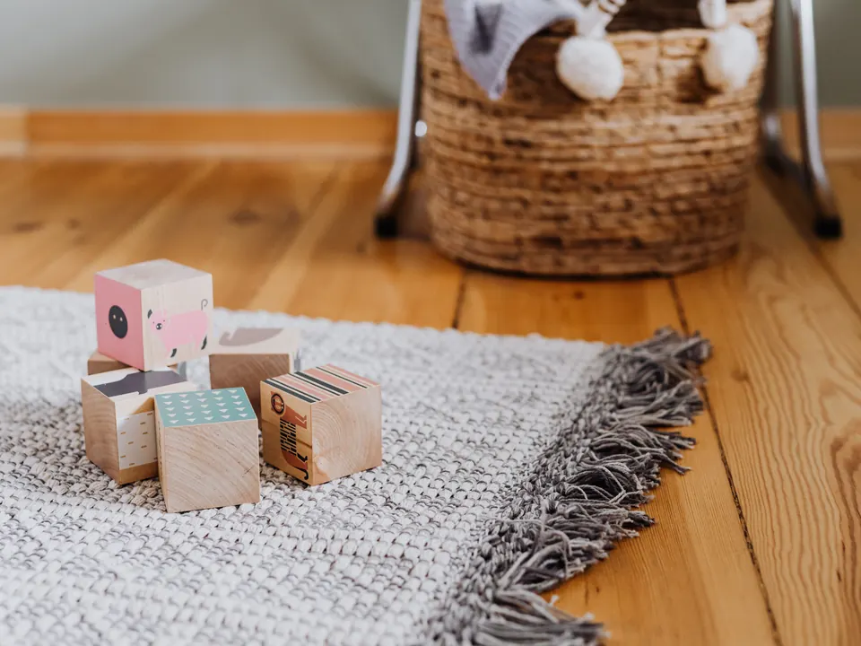 Houten blokjes met dierenprints op een wit kleed op een houten vloer, met een rieten mand erachter