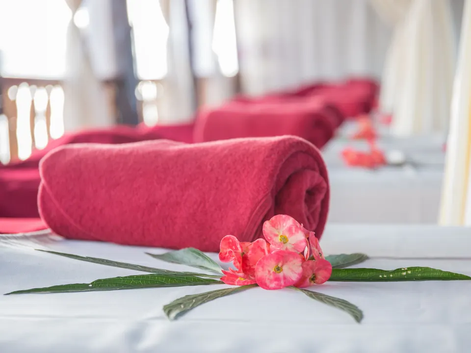 Opgerolde rode handdoek met bloemen op een massagetafel in een rustige behandelruimte