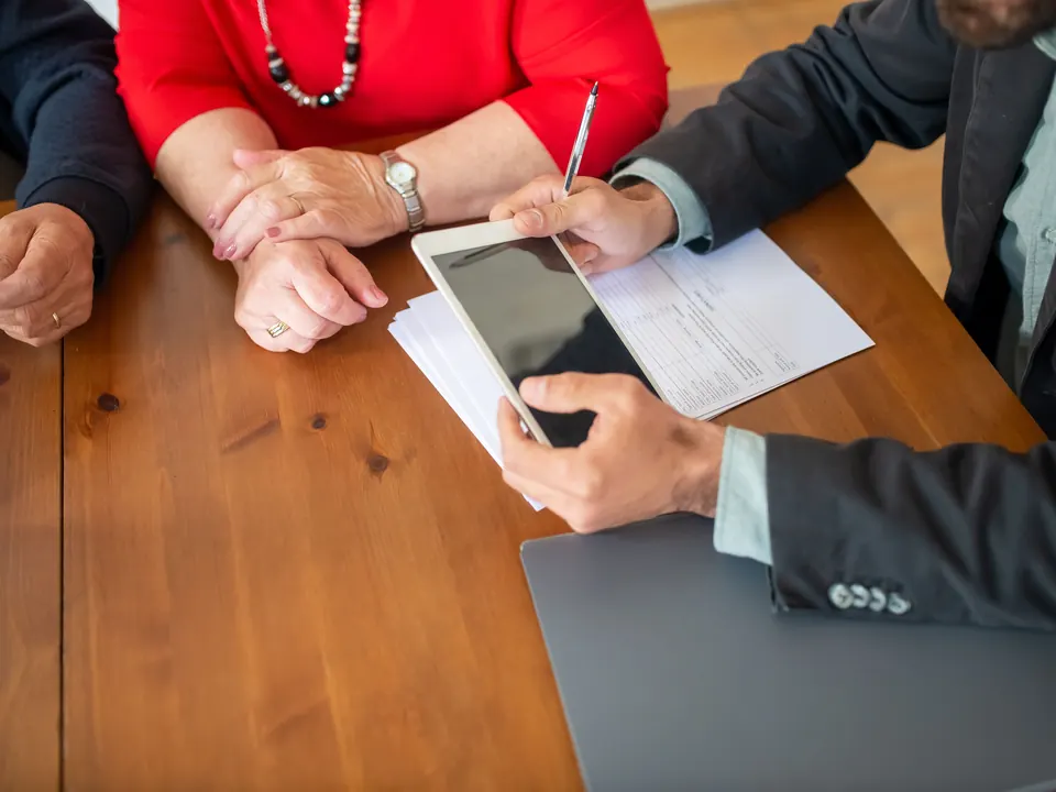 Adviseur bespreekt formulieren op een tablet met twee klanten aan een houten tafel